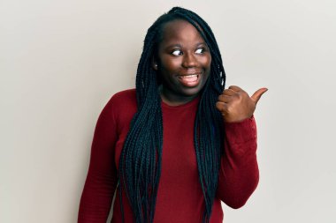 Saçları örgülü genç siyahi bir kadın başparmağını kaldırmış, ağzı açık gülümsüyor. 