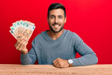 50 avroluk banknotlar tutan yakışıklı İspanyol adam. Olumlu ve mutlu görünüyor. Kendine güvenen bir gülümsemeyle dişlerini gösteriyor. 