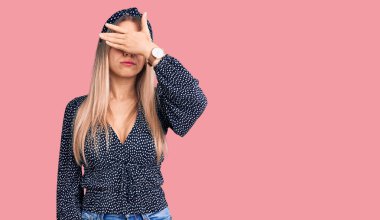 Genç, güzel, sarışın bir kadın. Günlük kıyafetler giyip, gözlerini eliyle kapatıyor. Ciddi ve üzgün görünüyor. Görme, saklama ve reddetme konsepti 