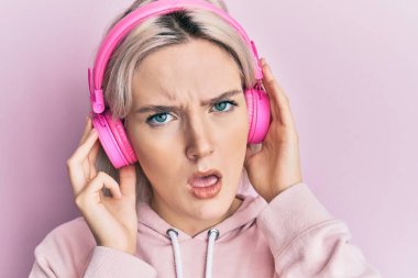 Genç sarışın kız müzik dinliyor. Kulaklıklarını takmış, kuşkucu, alaycı ve ağzı açık bakıyor. 