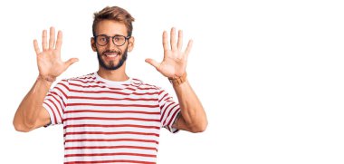 Sakallı, sıradan kıyafetler ve gözlük takan yakışıklı sarışın adam on numarayı gösterip işaret ederken kendinden emin ve mutlu gülümsüyor.. 