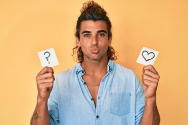 Genç İspanyol adam kalbi tutuyor ve soru işareti hatırlatıcısı kameraya bakıp öpüşürken sevimli ve seksi oluyor. aşk ifadesi. 