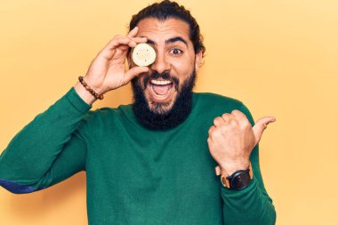 Genç Arap adam salatalık sümüğünü tutarken başparmağını yana doğru uzatıyor ve ağzı açık gülümsüyor. 