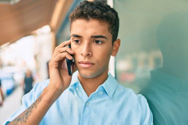 Ciddi bir suratı olan genç bir latin şehirde akıllı telefondan konuşuyor..