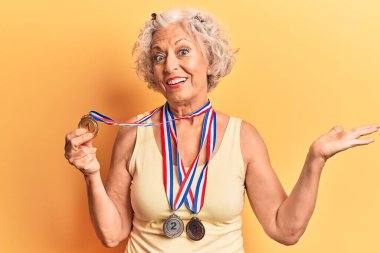 Başarı madalyalarını takan yaşlı gri saçlı kadın mutlu bir gülümsemeyle kutlama yapıyor ve kazanan yüz ifadesi kaldırıyor. 