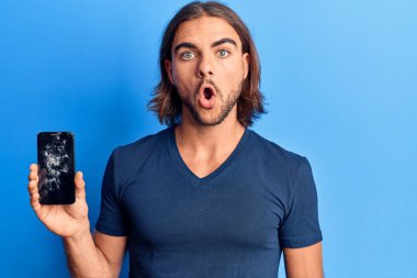 Kırık akıllı telefon tutan genç yakışıklı adam kırık ekranı gösteriyor korkmuş ve ağzı açık şaşırmış, inançsız yüz. 