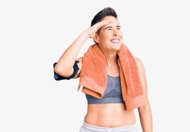 Kısa saçlı, spor giyimli ve havluyla akıllı telefon kullanan çok mutlu ve tebessüm eden genç bir kadın. arama kavramı. 