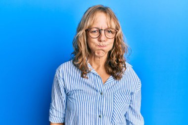 Sıradan kıyafetler giyen, gözlüklü, komik yüzlü, yanakları şişen orta yaşlı sarışın bir kadın. Havayla şişmiş ağız, çılgın bir ifade.. 