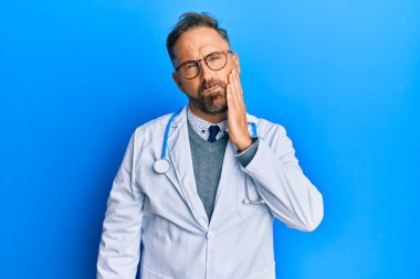 Doktor üniforması giyen yakışıklı orta yaşlı bir adam ve diş ağrısı ya da diş hastalığından dolayı ağız ve ellerle dokunan bir steteskop. dişçi 