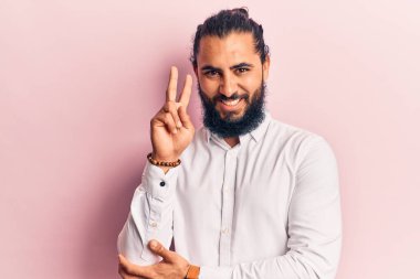 Gündelik kıyafetler giyen genç bir Arap kameraya gülümseyen ve zafer işareti yapan bir adam. İki numara.. 