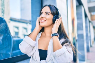 Genç İspanyol kız gülümseyerek şehirde kulaklık takarak müzik dinliyor..