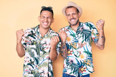 Yaz şapkası ve Hawaii tişörtü giyen iki genç gay kolları havada, gülümseyen ve başarı için çığlık atan kazanan hareketler yaparak çok mutlu ve heyecanlı. kutlama konsepti. 