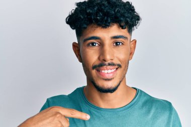 Gündelik giysiler giymiş genç Arap yakışıklı adam gülümseyen mutlu ve gururlu birini işaret ediyor. 