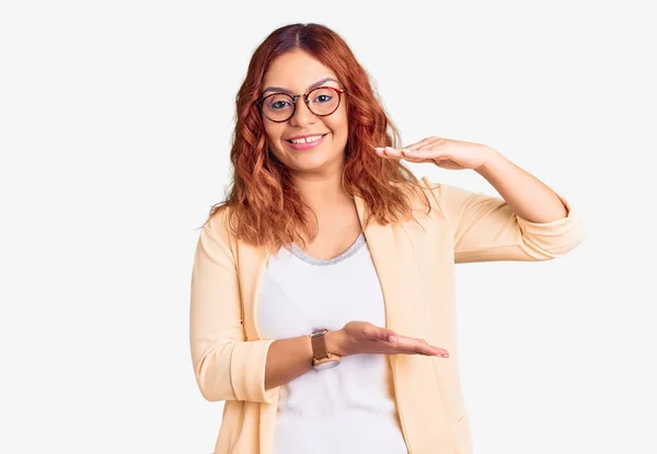 年轻的拉丁女人穿着商务服装 手拿着大号和大号的手势 测量符号 微笑着看着摄像机 计量概念 — 图库照片