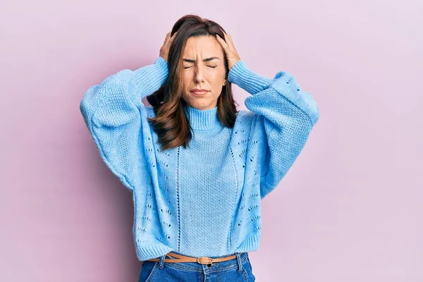 年轻的黑发女人穿着宽松的冬季毛衣 背景是粉色的 由于疼痛和偏头痛 绝望和紧张 手放在头上 — 图库照片