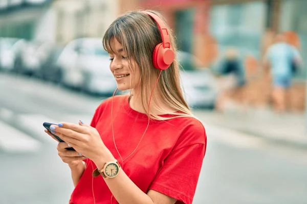 白人のティーンエイジャーの女の子笑顔幸せな使用してスマートフォンやヘッドフォンで街 — ストック写真