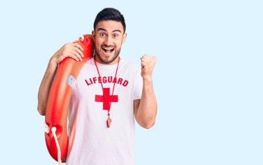 Cankurtaran üniforması giymiş genç yakışıklı adam elinde şamandırayla gururla bağırıyor zaferi kutluyor ve başarıyı kollarını kaldırarak kutluyor. 