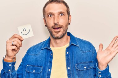 Gülümseme emojisi tutan genç yakışıklı adam başarıyı mutlu bir gülümsemeyle ve kazanan yüz ifadesiyle kutluyor. 