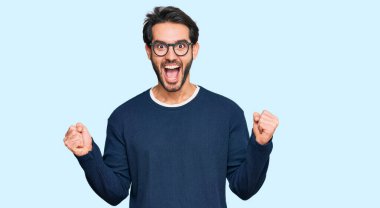 Gündelik kıyafet ve gözlük takan genç İspanyol adam kollarını kaldırıp, gözlerini açarak başarının şokunu yaşıyor ve hayrete düşüyor. Kazanan konsept. 