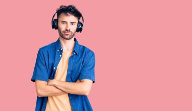 Genç İspanyol adam kulaklık takarak müzik dinliyor şüpheci ve gergin, yüzündeki ifadeyi onaylamıyor ve kollarını kavuşturuyor. negatif kişi. 