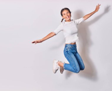 Saçları örgülü, sıradan kıyafetler giyen, mutlu gülümseyen genç ve güzel bir kadın. Yüzünde ve kollarında tebessümle atlayan izole beyaz arka planda açılan