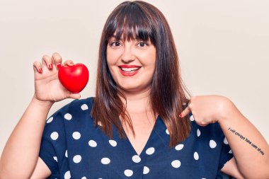 Genç ve cüsseli bir kadın kalbi tutuyor ve gülümseyen mutlu ve gururlu birini işaret ediyor. 