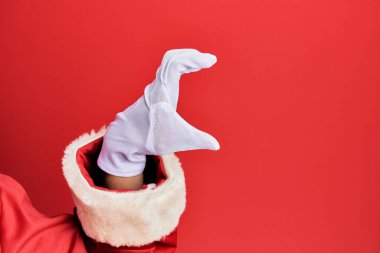 Elinde Noel Baba kostümü ve kırmızı arka plan eldivenleri olan görünmez bir şey tutan, parmakları yer gösteren bir adam. 