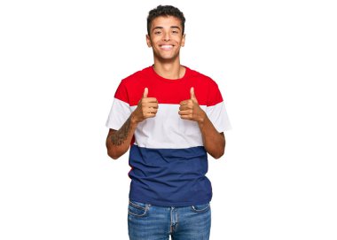 Genç, yakışıklı, Afro-Amerikan bir adam, günlük kıyafetler giyiyor, başarı işareti yapıyor, elleriyle olumlu jest yapıyor, gülümsüyor ve mutlu. Neşeli ifade ve kazanan jest. 