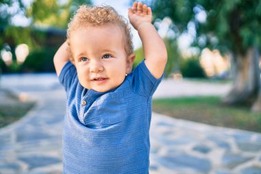 Sevimli ve mutlu küçük çocuk güneşli bir günde parkta eğleniyor. Güzel sarı saçlı erkek çocuk dışarıda oynuyor.