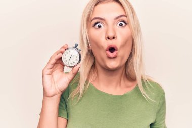 Young beautiful blonde woman doing countdown using stopwatch over white background scared and amazed with open mouth for surprise, disbelief face