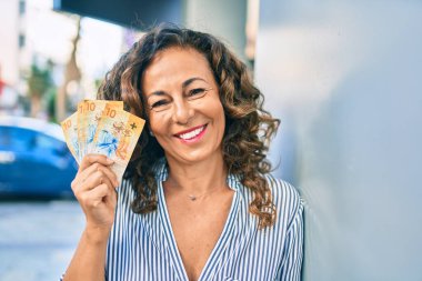 Orta yaşlı İspanyol kadın gülerek şehirde İsviçre frangı banknotları tutuyor..