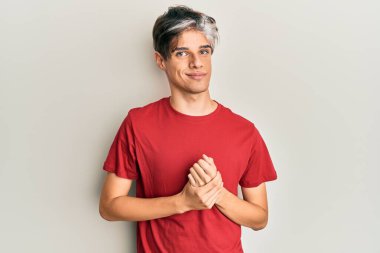 Latin asıllı genç adam ellerinin birleştiği günlük kıyafetler giyiyor ve gülümseyerek gevşemiş ve neşeli gülümsüyor. Başarı ve iyimserlik 