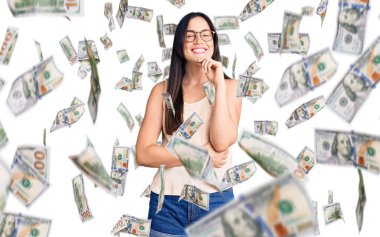 Gündelik kıyafetler ve gözlük takan genç beyaz bir kadın kameraya kendinden emin bakıyor kolları çapraz ve çenesi açık gülümsüyor. Olumlu düşünmek.