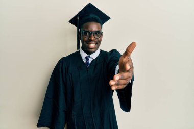 Mezuniyet şapkası ve tören cübbesi takan yakışıklı siyahi adam selamlama ve hoş geldin demek için dostça tokalaşıyor. başarılı iş. 