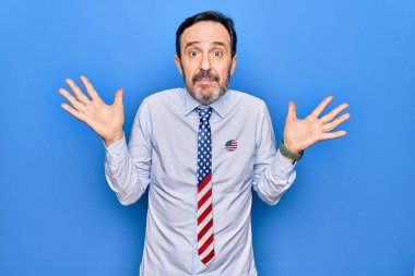 Orta yaşlı, vatansever, Amerika Birleşik Devletleri 'ne bağlı yakışıklı bir iş adamı mavi arka planda hiçbir şey bilmiyor ve kolları açık, hiçbir fikri yok ve şüpheli bir yüzü var..