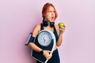 Kilo kaybetmeyi dengelemek için elinde ağırlık makinesi tutan genç, güzel, kızıl saçlı bir kadın sinirli ve öfkeli çığlıklar atıyor. Öfkeyle bağırıyor. öfke ve agresif konsept. 