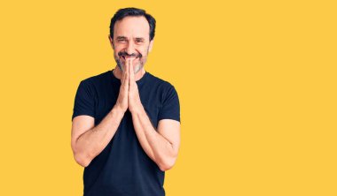 Orta yaşlı yakışıklı bir adam sıradan bir tişört giyip ellerinin birarada dua ederek af diliyor kendinden emin bir şekilde gülümseyerek.. 