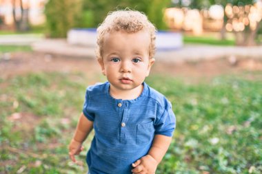 Sevimli ve mutlu küçük çocuk güneşli bir günde parkta eğleniyor. Güzel sarı saçlı erkek çocuk dışarıda oynuyor.