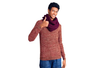 Genç Afro-Amerikan adam, günlük kışlık kazak ve eşarp giyerek mutlu bir el hareketi yapıyor. Kameraya bakıp başarıyı gösteren ifade. 