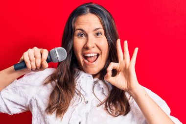 Genç, güzel esmer kadın mikrofon kullanarak şarkı söylüyor. Parmaklarıyla işaret veriyor, gülümsüyor. Mükemmel bir sembol.