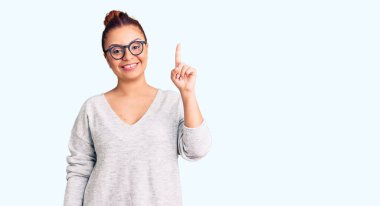 Gündelik kıyafetler giyen genç Latin kadın bir numarayı gösterip işaret ederken kendinden emin ve mutlu bir şekilde gülümsüyor.. 