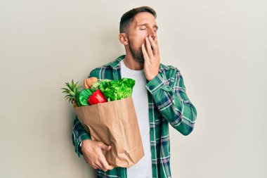 Elinde poşetle sakallı yakışıklı bir adam market alışverişi yapmaktan sıkılmış, ağzı eliyle kapatmaktan sıkılmış. Huzursuz ve uykulu.. 