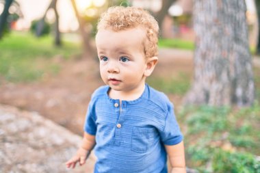 Sevimli ve mutlu küçük çocuk güneşli bir günde parkta eğleniyor. Güzel sarı saçlı erkek çocuk dışarıda oynuyor.