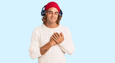 Genç İspanyol adam müzik dinliyor kulaklık takıyor elleri göğsünde, gözleri kapalı gülümsüyor ve yüzünde minnet ifadesi var. sağlık kavramı. 