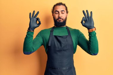 Berber önlüğü giyen genç Arap adam rahatla ve parmaklarıyla meditasyon hareketi yaparken gözleri kapalı gülümse. yoga konsepti. 