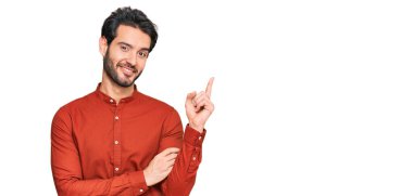 Yüzünde kocaman bir gülümseme olan, gündelik kıyafetler giyen genç İspanyol adam, kameraya el ve parmak ile bakıyor.. 