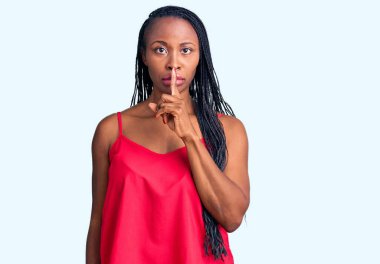 Genç Afro-Amerikalı kadın, günlük kıyafetler giyip dudaklarında parmaklarıyla sessiz olmak istiyor. sessizlik ve gizli konsept. 