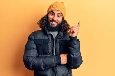 Gündelik kışlık kıyafetler giyen genç Arap adam gülümsüyor mutlu bir şekilde elini ve parmağını yana uzatıyordu. 