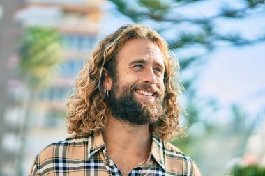 Parkta gülümseyen uzun saçlı beyaz bir genç..