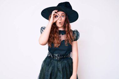 Cadı cadılar bayramı kostümü giyen genç ve güzel bir kadın. Şaşırmış bir yüz ve parmaklarından bakan bir gözle şaşırmış bir jest yapıyor. İnançsız ifade. 